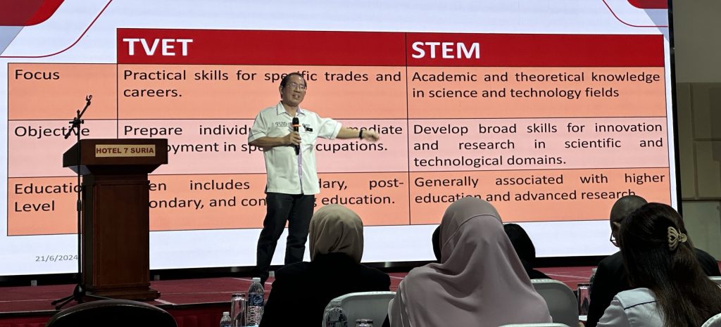 A speaker presenting a comparison between TVET and STEM education pathways during an event in Sabah, with attendees listening attentively.